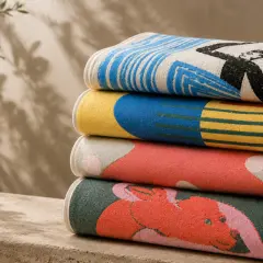 Pile de serviettes aux motifs graphiques colorés, réalisées en tissu jacquard. L'une représente une silhouette noire sur fond rayé bleu et blanc.