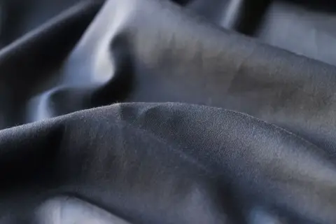 Plis du polyester tissu, d'une teinte gris foncé, créant des ombres douces et des reflets subtils.