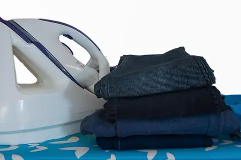 Fer à repasser et pile de vêtements sombres sur une planche à repasser. Apprenez comment repasser du polyester pour un résultat impeccable.