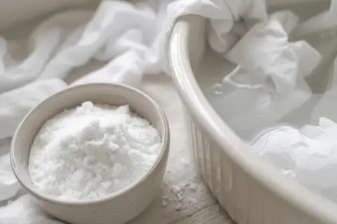 Poudre blanche dans un bol, prête à blanchir un vêtement trempé dans une bassine d'eau.