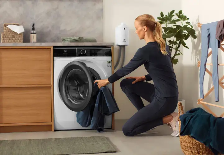 Femme chargeant du linge dans une machine, dont un vêtement en matière PBT, dans une buanderie moderne.