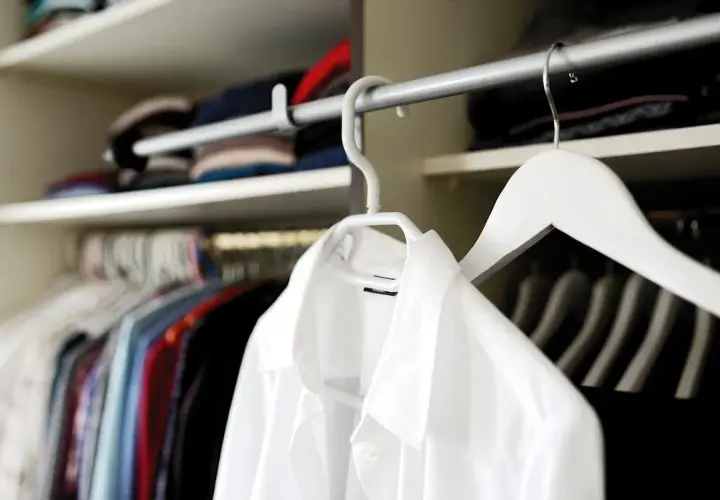 Chemises colorées et une chemise blanche en polyester, suspendues dans une penderie.