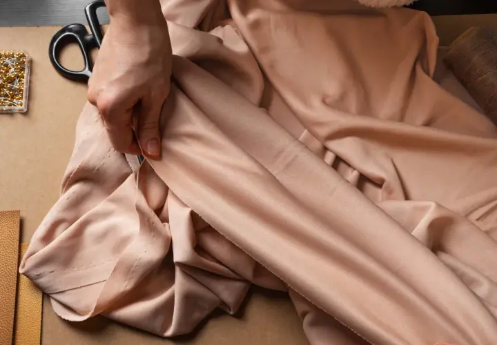 Mains tenant un tissu fluide de viscose été. Ciseaux, épingles et fil à portée de main pour la création.