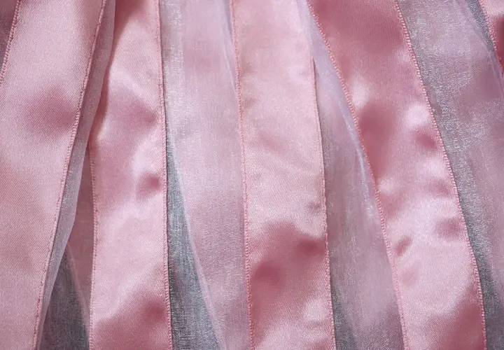 Bandes verticales de tissu brillant rose et argenté, créant un effet de texture doux et lumineux.