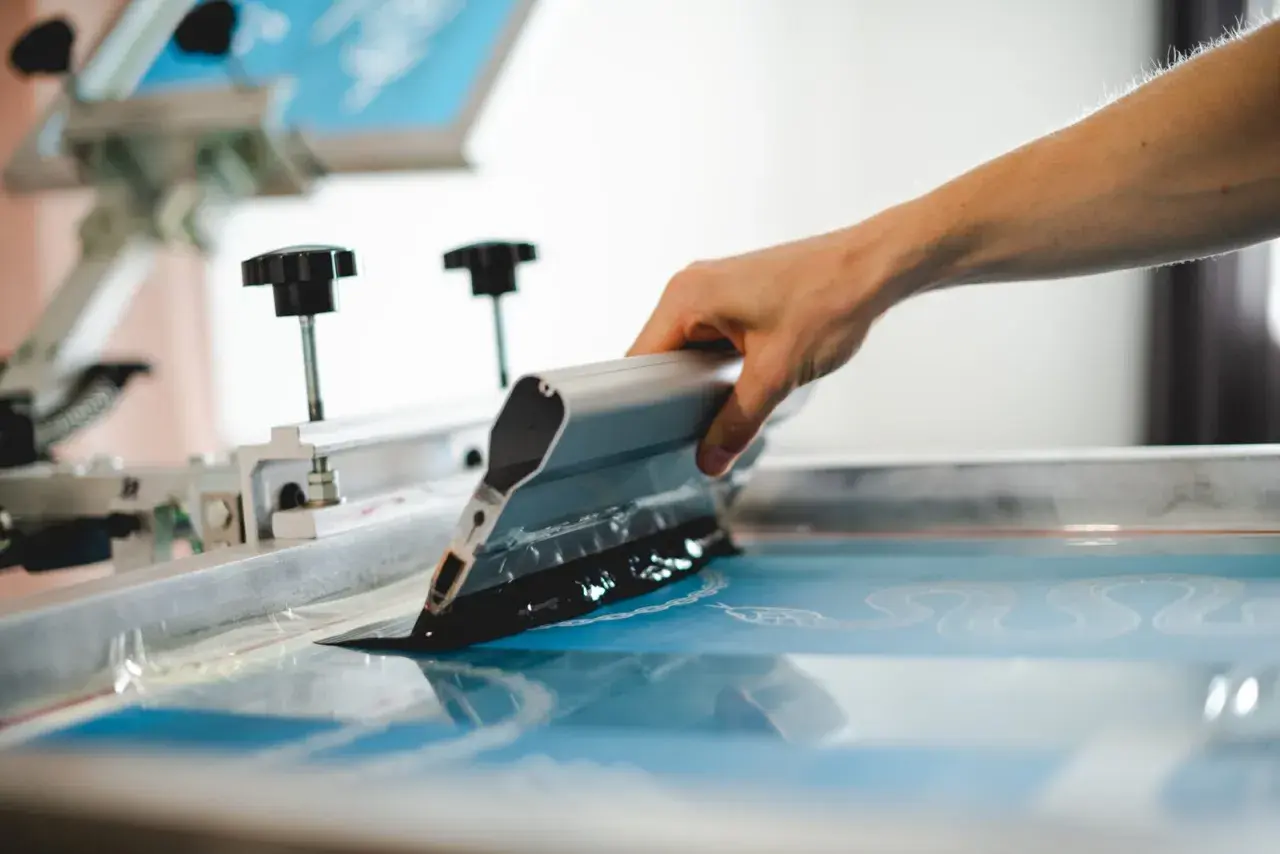 Main d'artisan appliquant de l'encre sur un écran pour la sérigraphie textile. Le motif commence à apparaître.