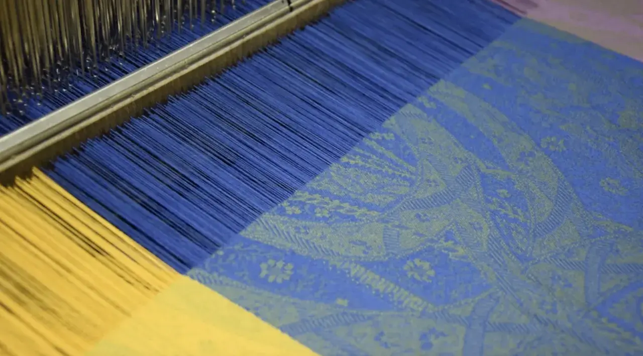 Le métier à tisser jacquard crée un motif complexe sur du tissu bleu et jaune.