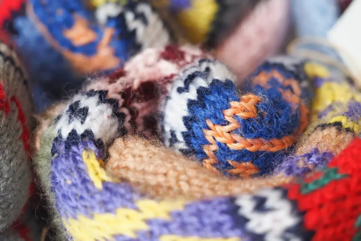 Gros plan sur un tissu jacquard aux motifs géométriques colorés, avec des fils de laine bleus, violets, jaunes et rouges entrelacés.