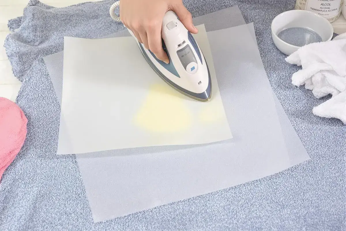 Utilisation d'un fer &agrave; repasser pour enlever colle thermocollant sur tissu, avec du papier sulfuris&eacute; pour prot&eacute;ger.
