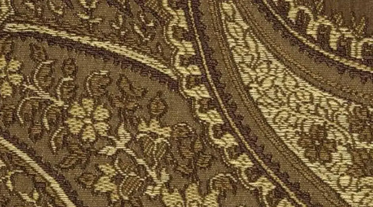 Gros plan sur un tissu jacquard aux motifs floraux et arabesques dans des tons de marron et beige, évoquant une richesse historique.
