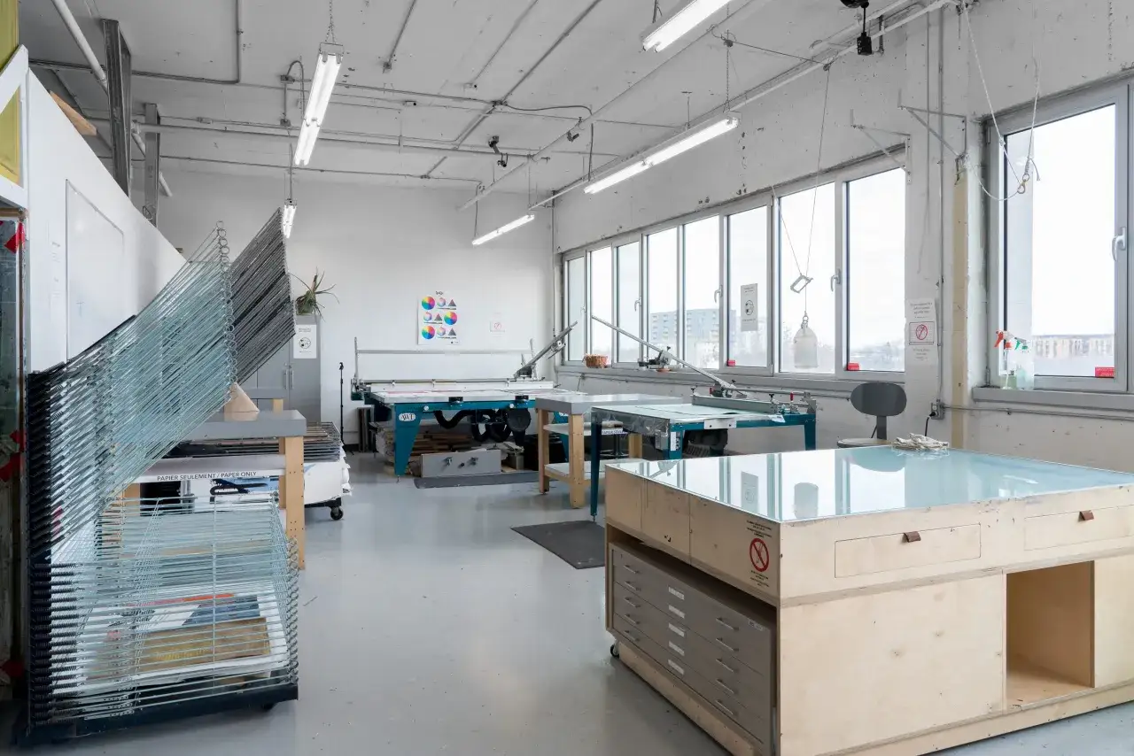 Atelier de sérigraphie textile avec tables d'impression, séchoir à racks et matériel d'art.