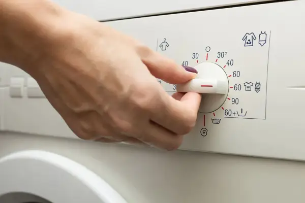 Main d'une personne réglant le bouton d'une machine à laver pour le lavage de vêtements.