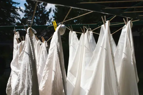 Des linges blancs, dont un pantalon, sèchent au soleil. Une astuce pour savoir comment blanchir un pantalon blanc : le laisser sécher à l'air libre après un bon lavage.